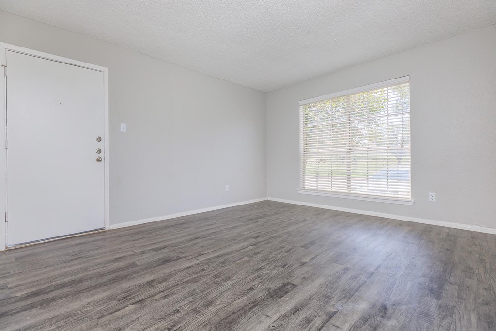 an empty living room with wood flooring and a window