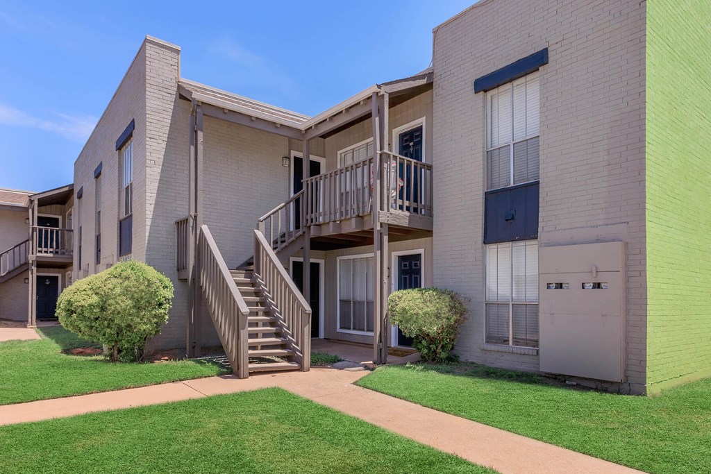 the exterior of an apartment building with stairs and grass