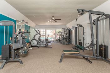 a gym with weights and cardio machines and a ceiling fan