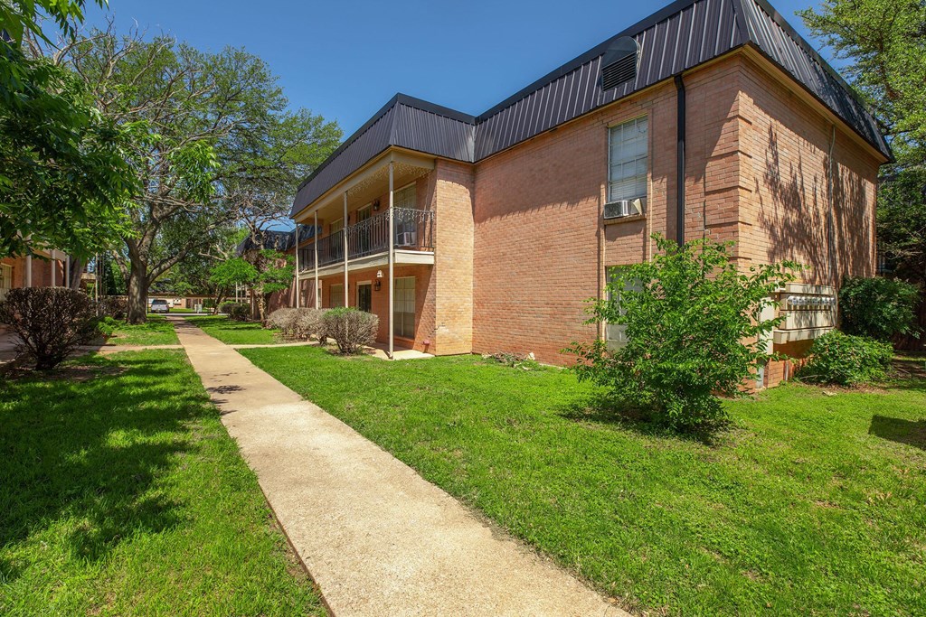 a sidewalk in front of a brick building with grass and trees