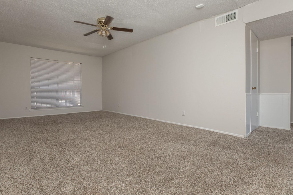 an empty living room with carpet and a ceiling fan