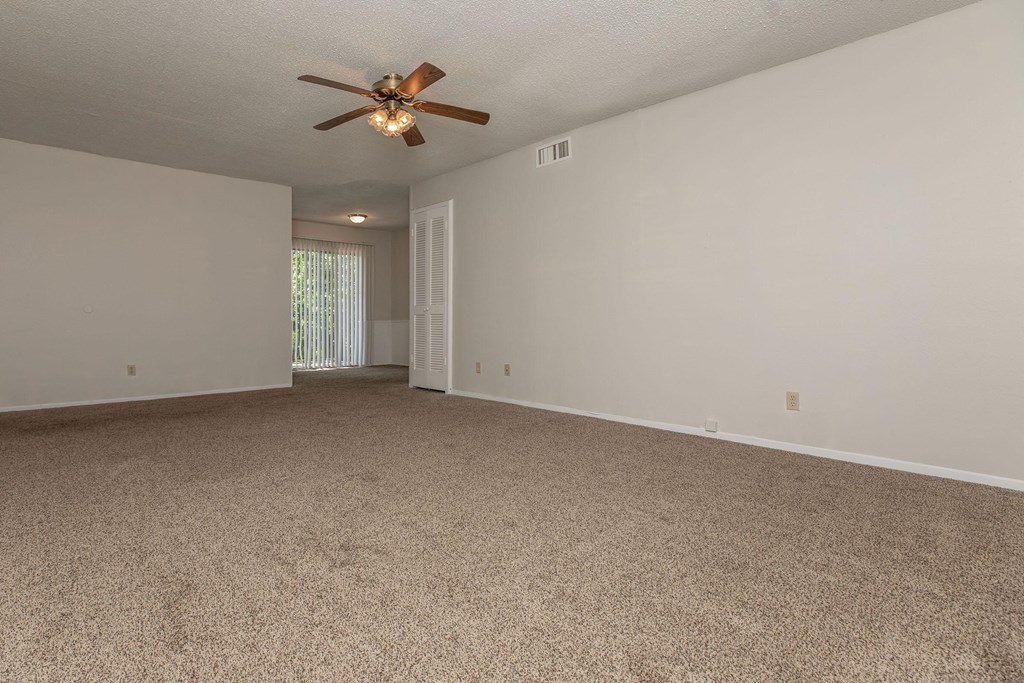 a spacious living room with carpet and a ceiling fan