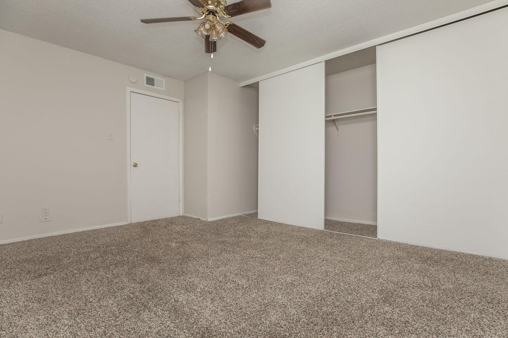 an empty living room with a ceiling fan and closet