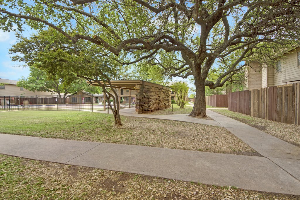 a sidewalk in a park with trees and a building