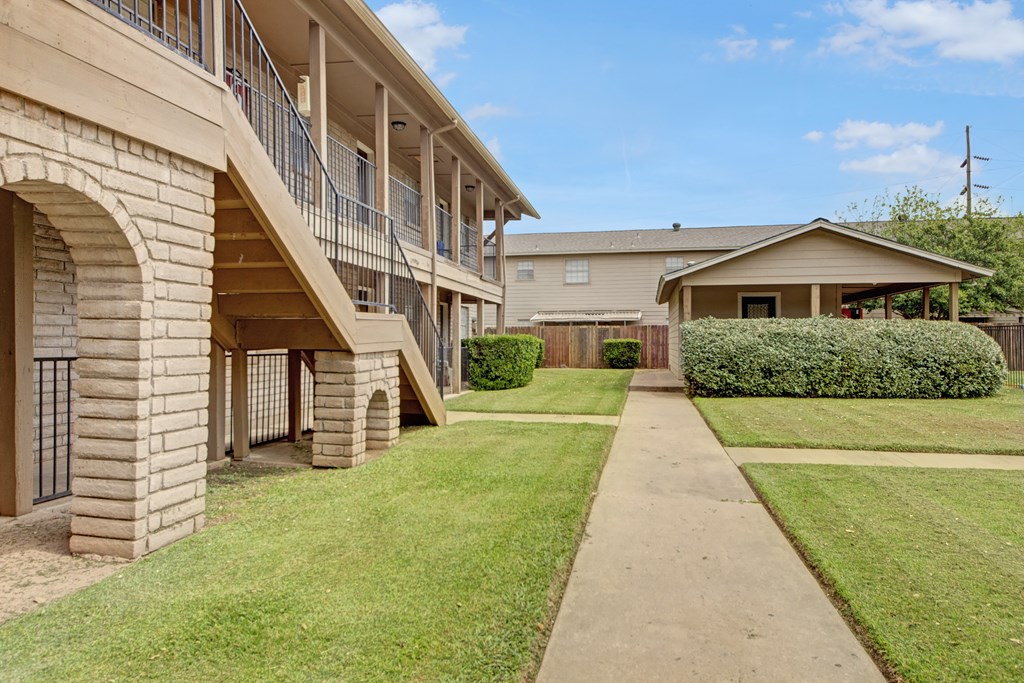 a sidewalk in front of a building with a yard and stairs