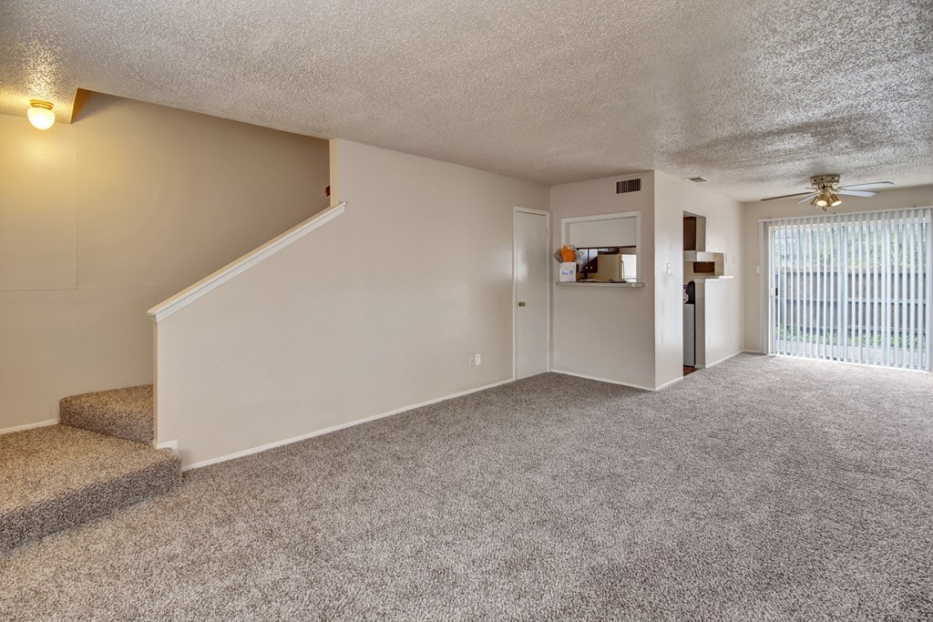 the spacious living room and entryway of an apartment with carpeted stairs and a