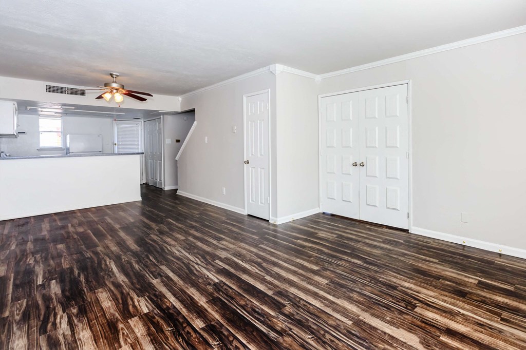 an empty living room with a kitchen and a ceiling fan