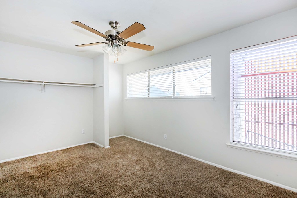 a bedroom with a ceiling fan and two windows