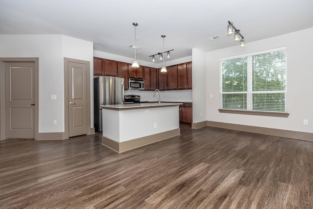 an empty living room with a kitchen with a refrigerator and a sink