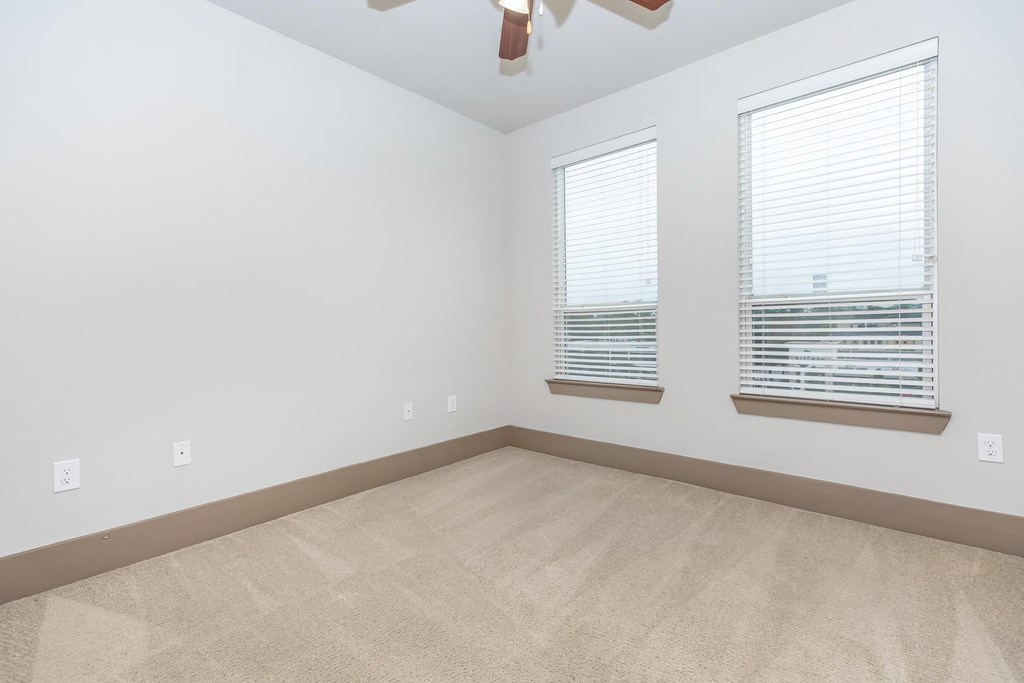 an empty room with three windows and a ceiling fan