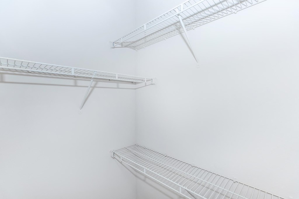 a walk in closet with white walls and shelves and a mirrored closet door