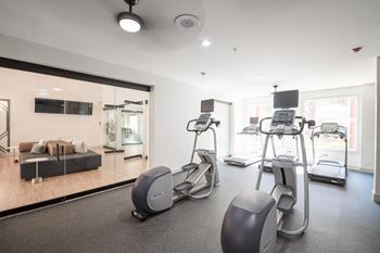 the gym is equipped with cardio equipment and a large mirror