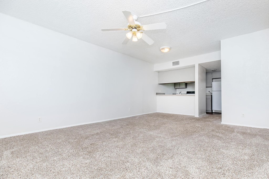 an empty living room with a ceiling fan and a kitchen