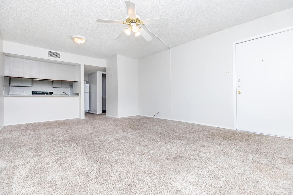 an empty living room with a ceiling fan and a kitchen