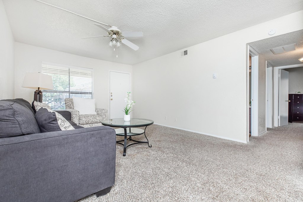 A living room with a grey couch, a small table, and a ceiling fan.