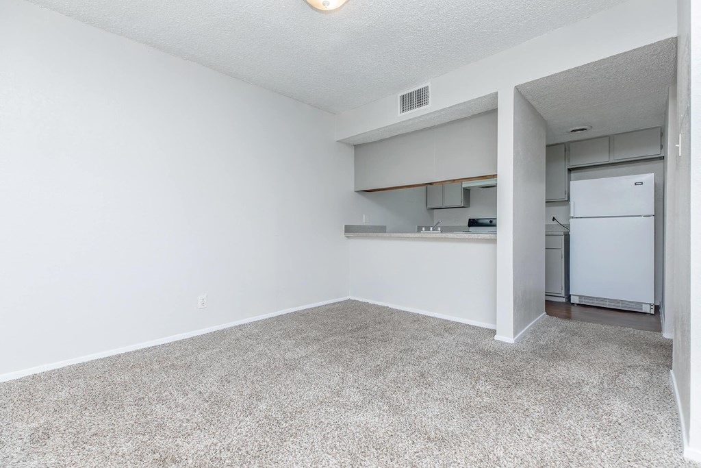 A white room with a carpeted floor and a white refrigerator in the corner.