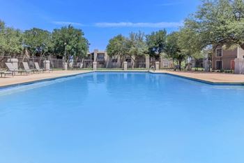 a large swimming pool with trees and apartments in the background