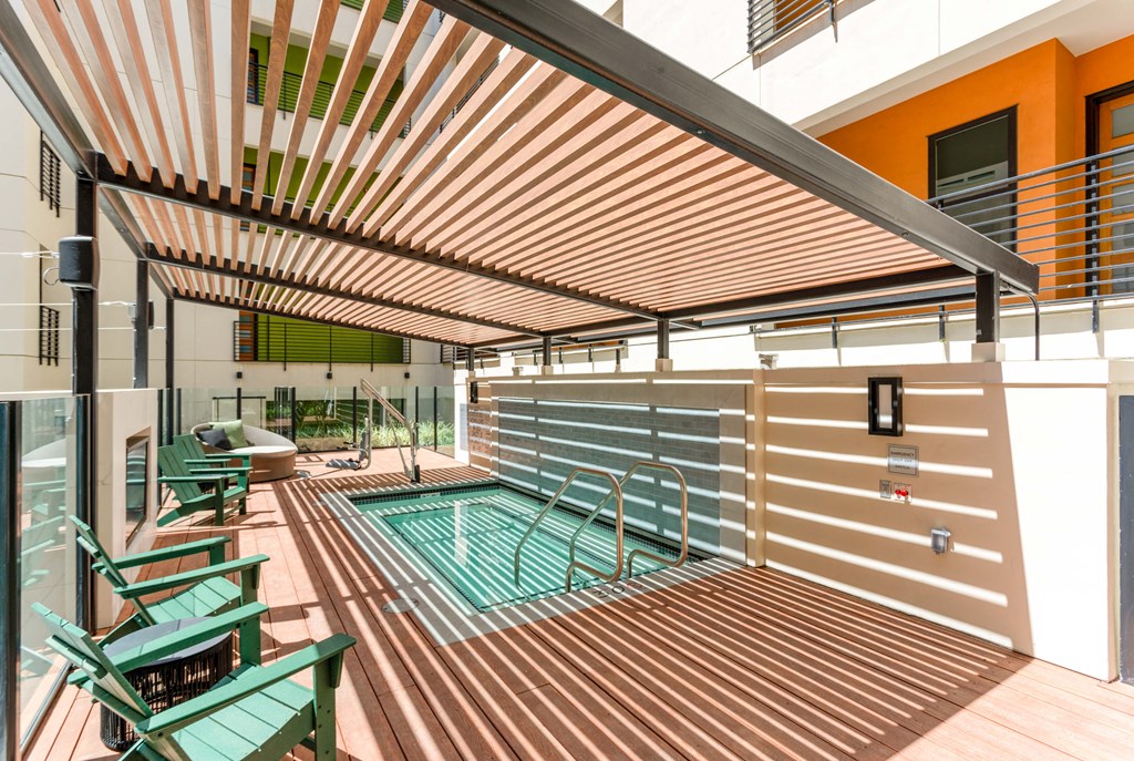 the pool area of a building with a pool and deck with green chairs