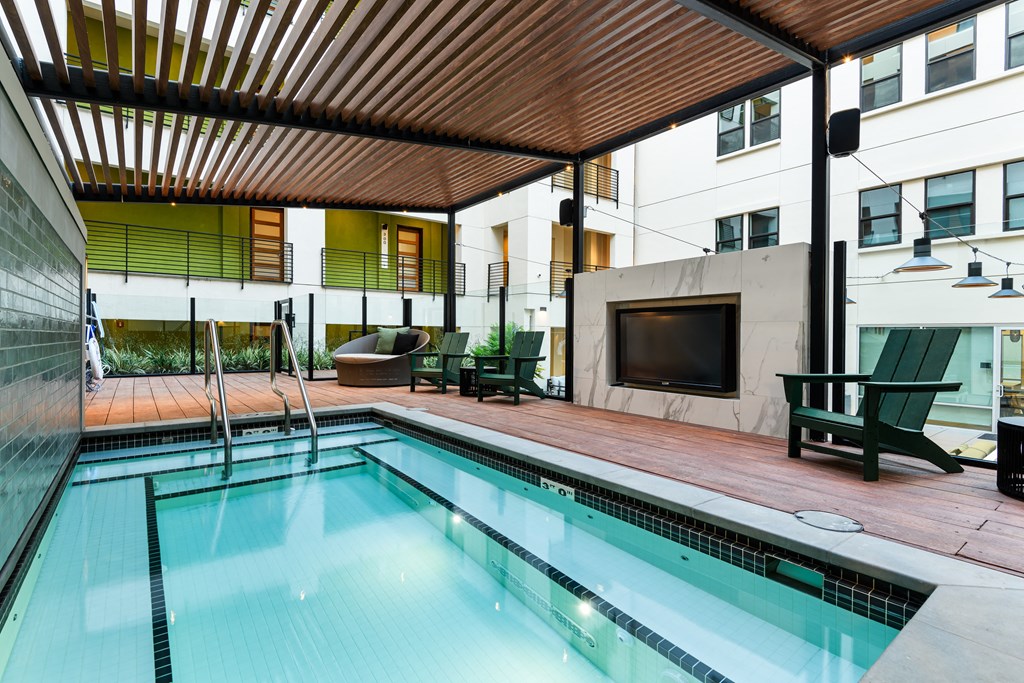 A swimming pool with a wooden ceiling and a TV on the wall.