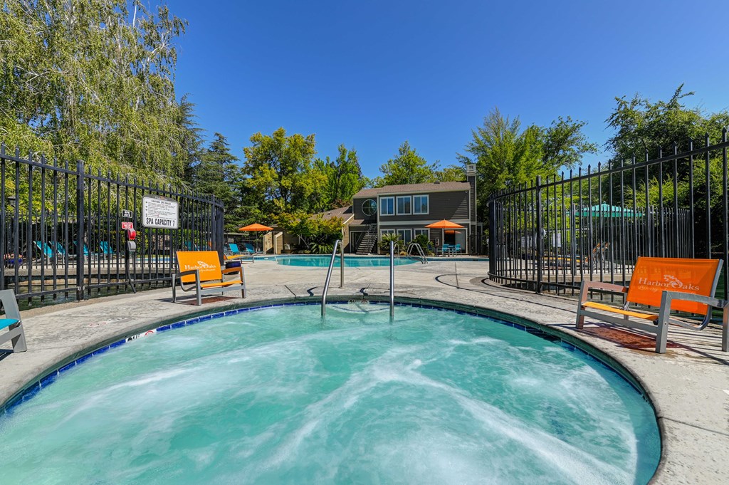 A hot tub is surrounded by chairs and a fence.