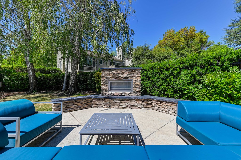 A blue couch and table are in the foreground of a backyard with a stone fireplace.