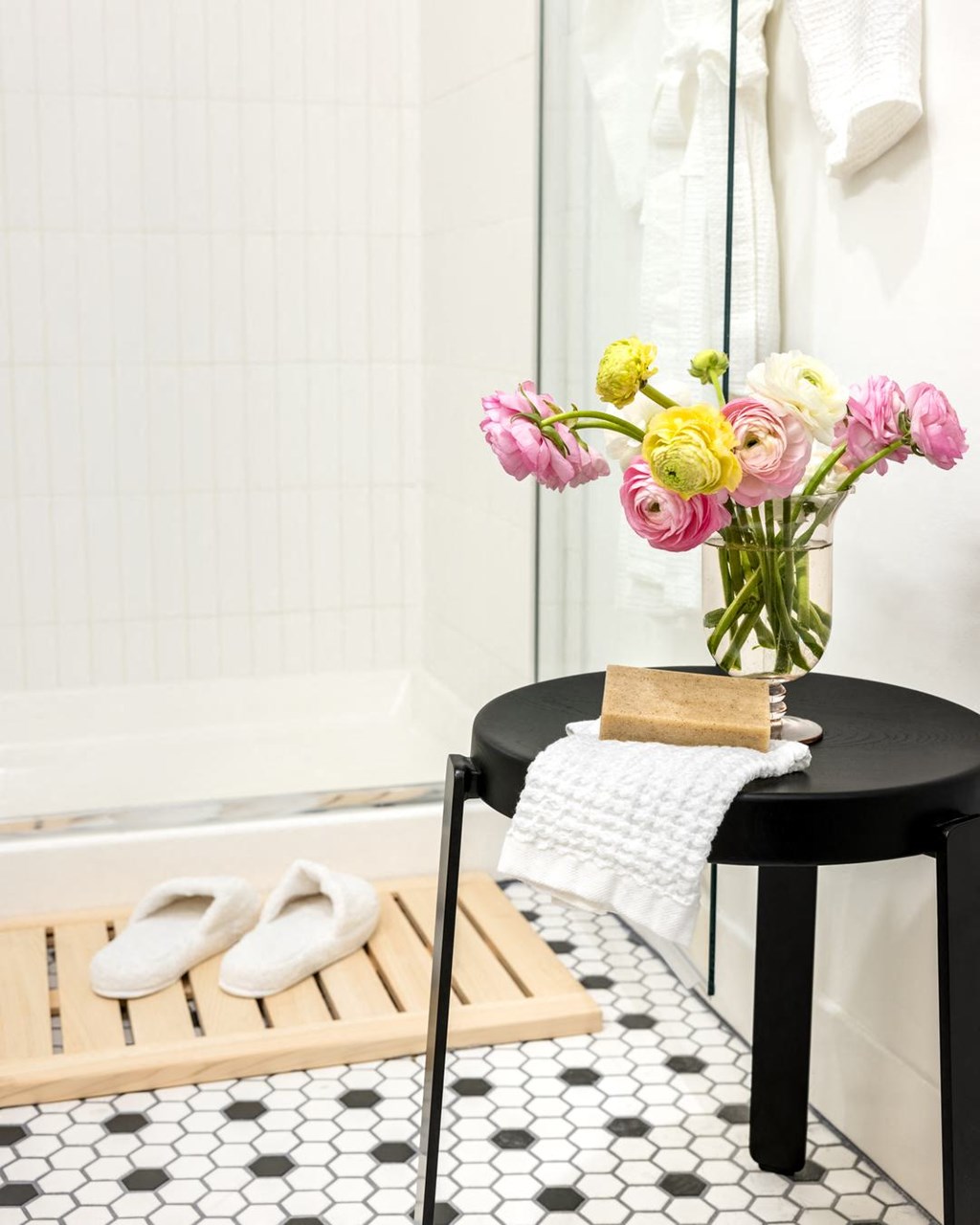 a bathroom with a black stool and a vase with flowers