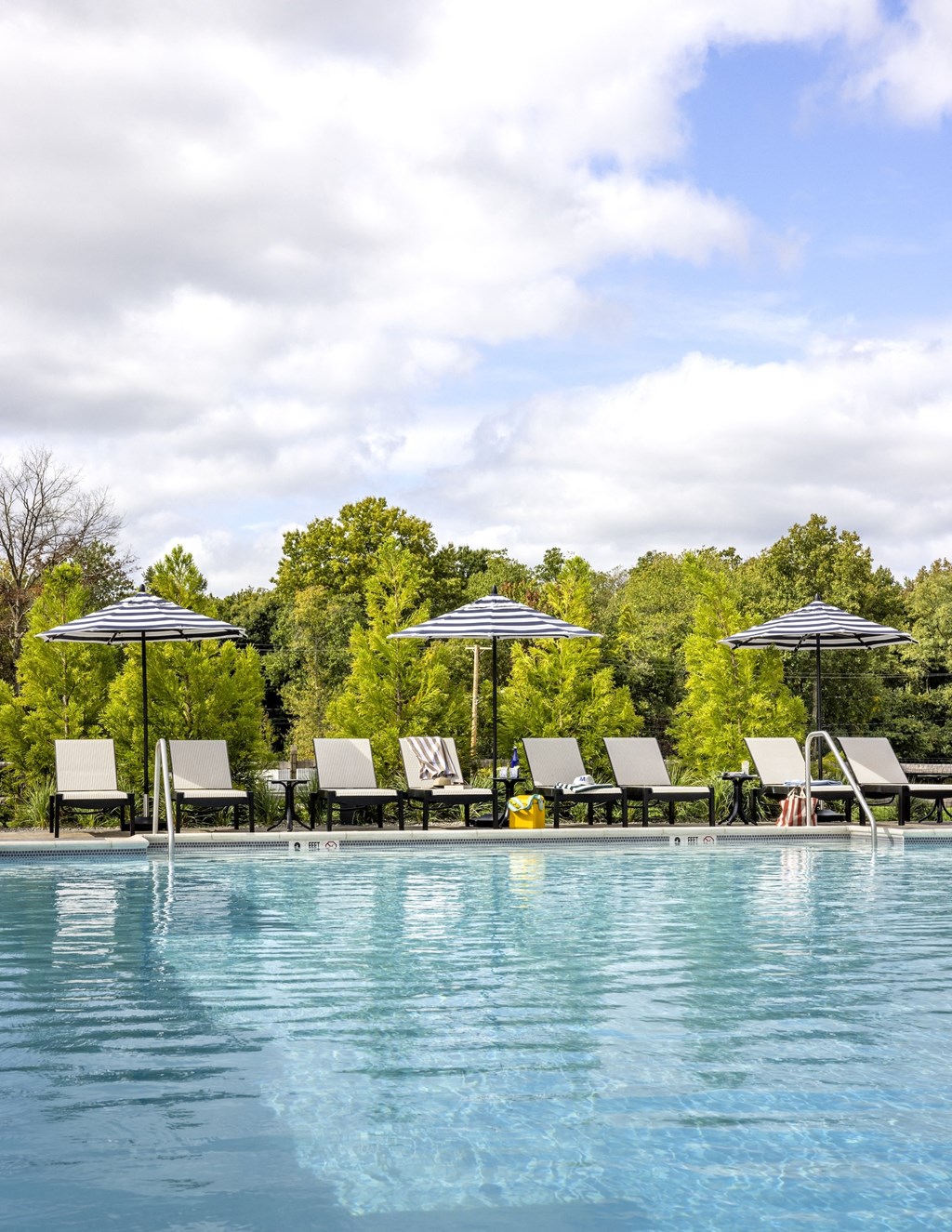 A pool with chairs and umbrellas in front of trees.