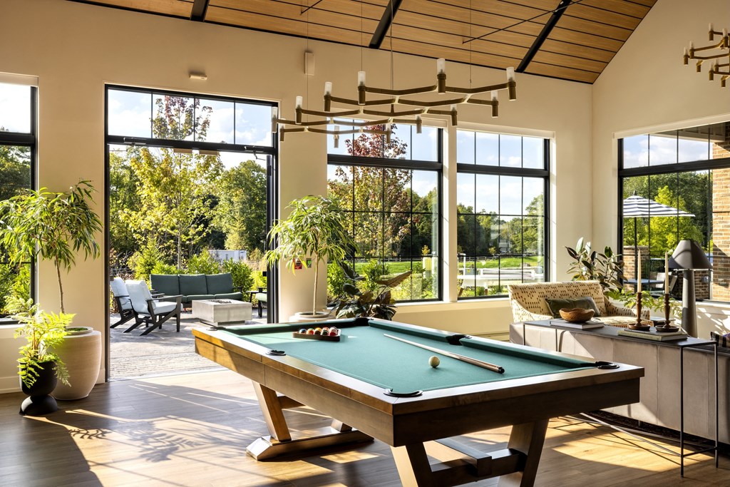 A pool table is in the middle of a room with a view of the trees outside.