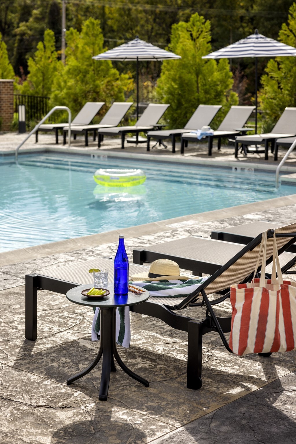 A poolside table with a hat, a bottle, a plate of food, and a bag.