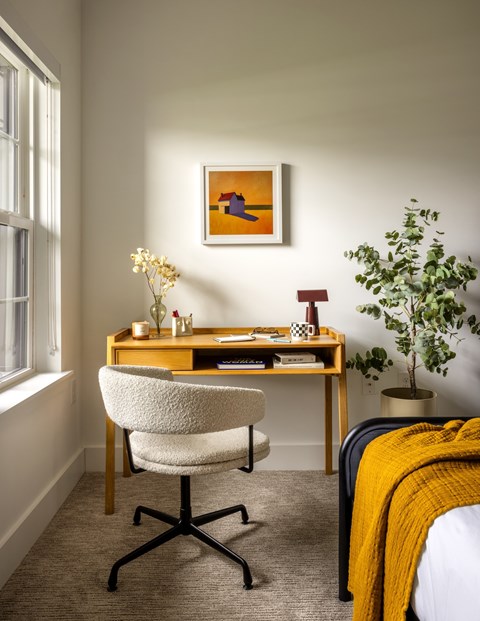 A room with a desk, chair, and a painting on the wall.
