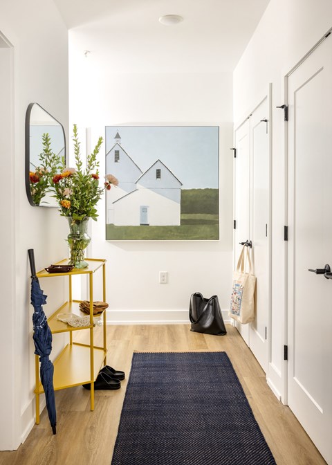A hallway with a yellow shelf and a painting of a house on the wall.