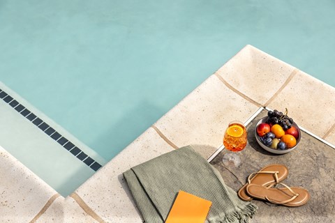A poolside setting with a towel, flip flops, and a bowl of fruit.