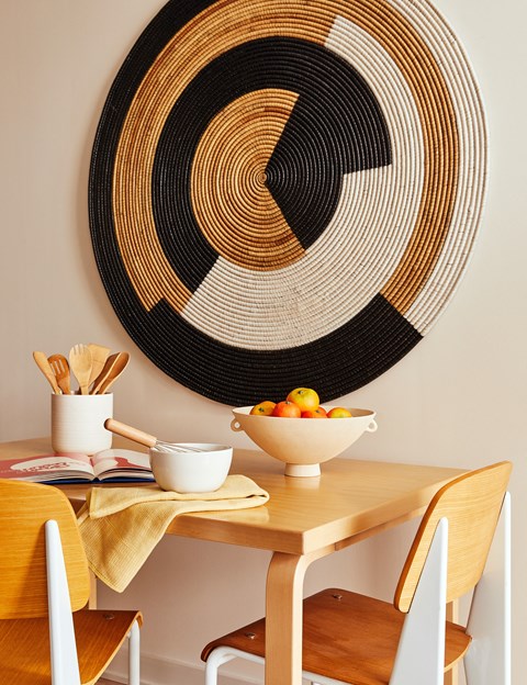a wooden table with a bowl of fruit on it and a wall art of a