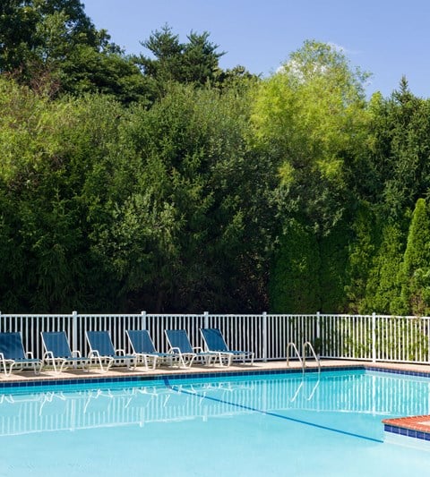 a swimming pool with blue chairs next to a white fence