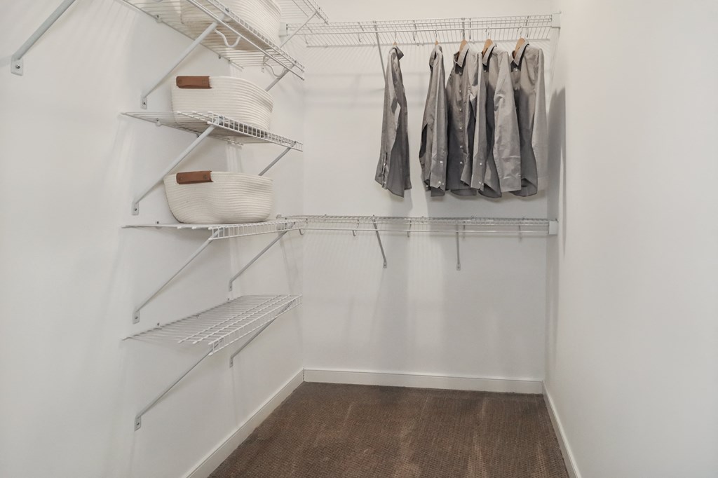 a walk in closet with white walls and shelves and a hanging rack with clothes