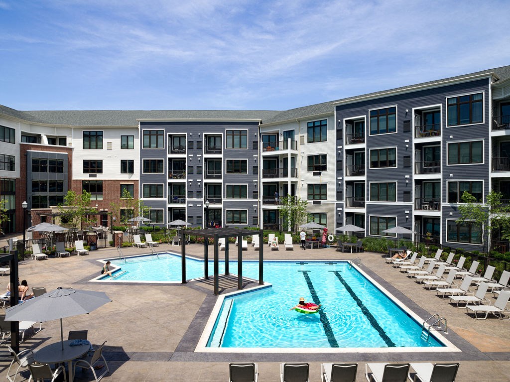 an apartment pool with chairs and umbrellas in front of an apartment building