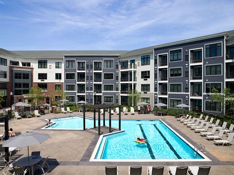 an apartment pool with chairs and umbrellas in front of an apartment building