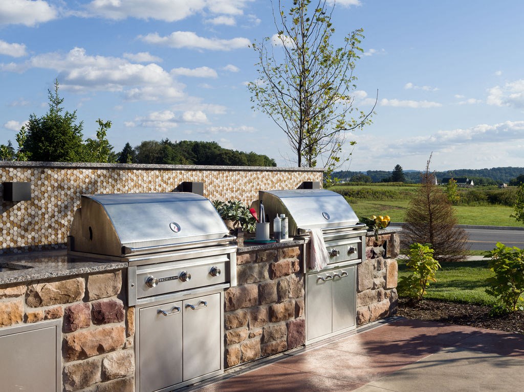 an outdoor kitchen with two stainless steel appliances and two bbqs