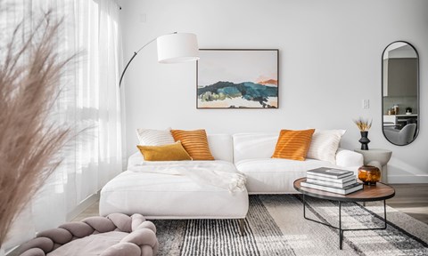 A modern living room with a white sofa, a grey rug, and a painting on the wall.