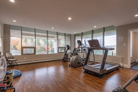an exercise room with cardio equipment and large windows