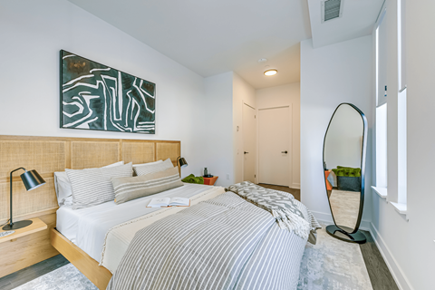 A bedroom with a bed, a lamp, a mirror and a painting on the wall.