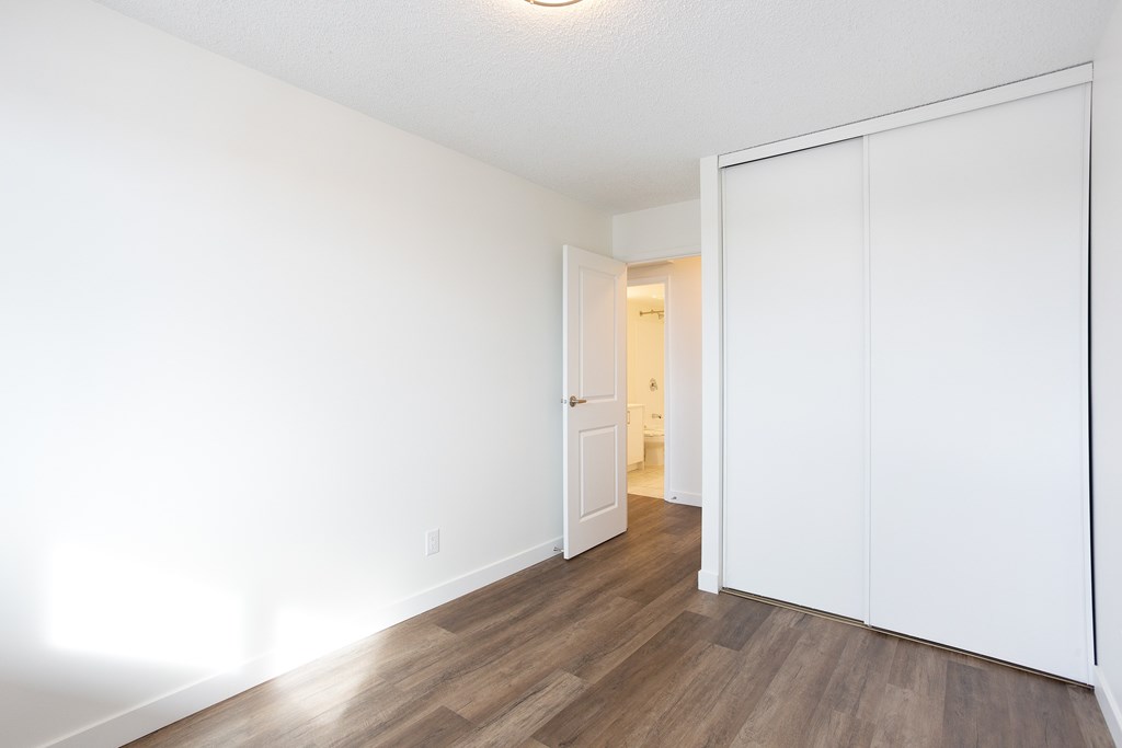 A room with white walls and wooden flooring with a white door.