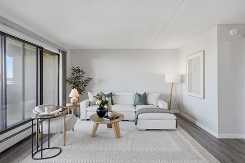 A modern living room with a white sofa, a wooden coffee table, and a glass table.