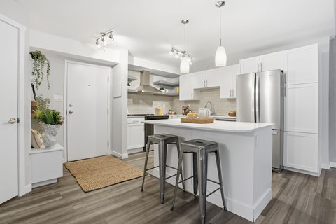 A kitchen with white cabinets and a white island with a refrigerator on the right side.