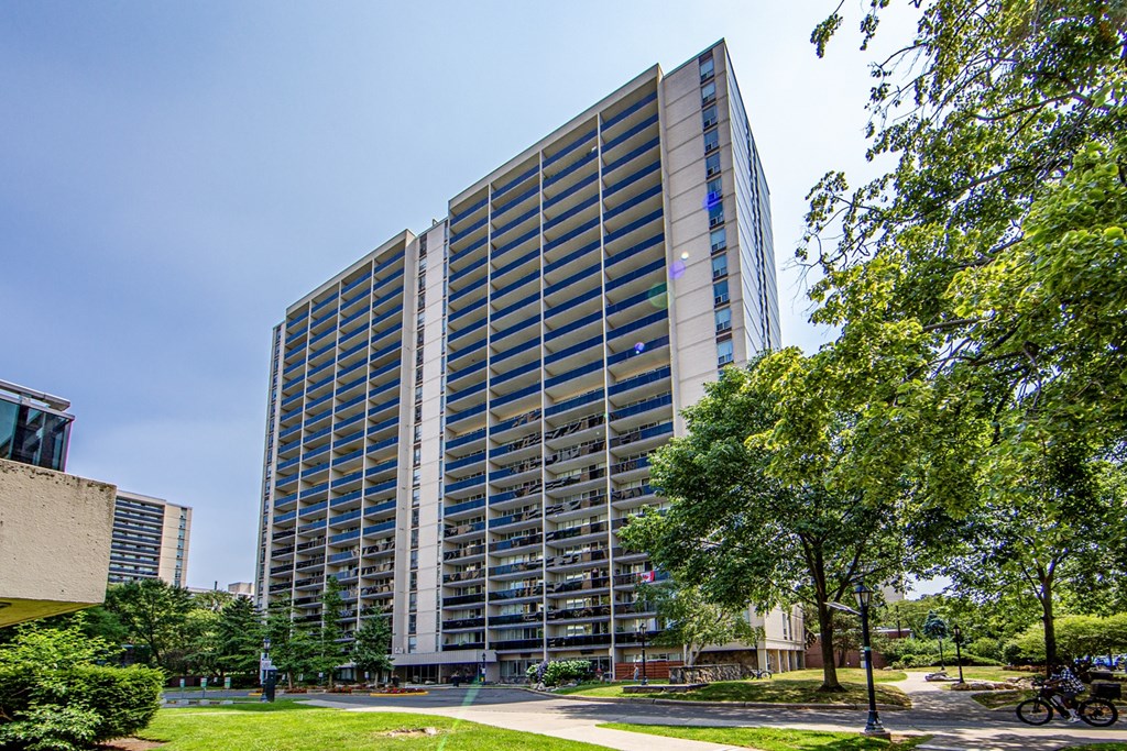 A tall building with many windows is surrounded by trees and greenery.