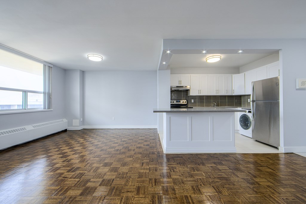 A kitchen with a refrigerator, stove, and cabinets is visible from a living room.