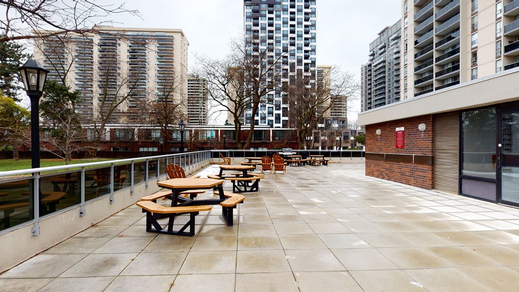 A patio with tables and benches is surrounded by buildings.