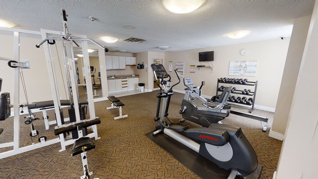 a gym with various machines and weights in a room with a kitchen