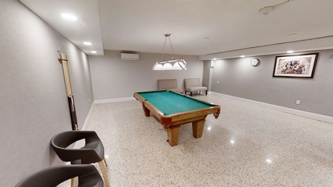A room with a pool table and chairs.