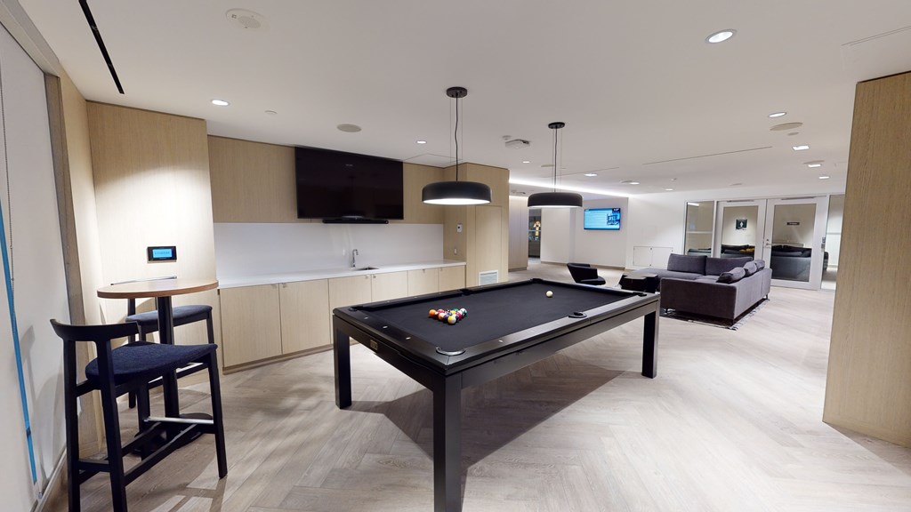 A pool table is in the middle of a room with a bar and a television.
